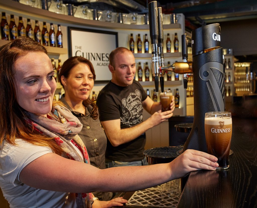 People behind a bar pouring pints of Guinness.